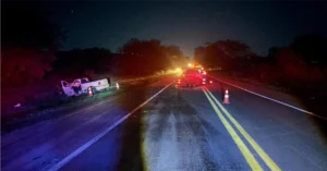 Visão geral de rodovia em pista simples com viatura policial no acostamento após colisão frontal na BR-369 em Andirá