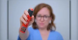 Mulher desfocada aponta um spray de pimenta em direção ao centro da imagem. Foto ilustrativa sobre a Lei 15.474, que autoriza a comercialização do dispositivo para defesa pessoal de mulheres maiores de 18 anos.