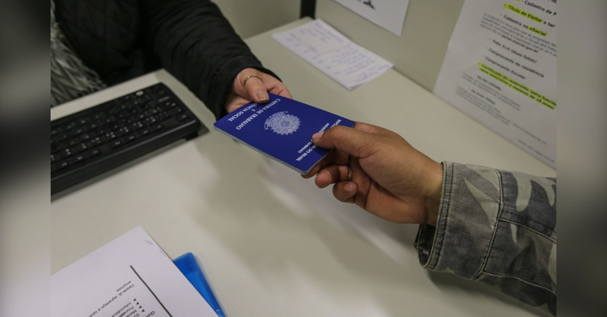 Mãos de duas pessoas trocando o documento da Carteira de Trabalho durante seleção para vagas de emprego em Maringá na Agência do Trabalhador.